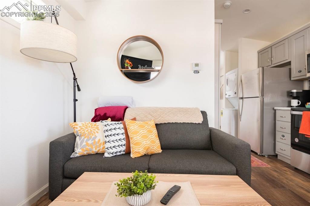 Image 13 of 27: Living area with dark wood-style floors, baseboards, and stacked washer / d