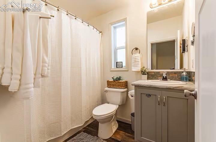 Image 19 of 27: 3/4 bathroom with tasteful backsplash, toilet, vanity, wood finished floors
