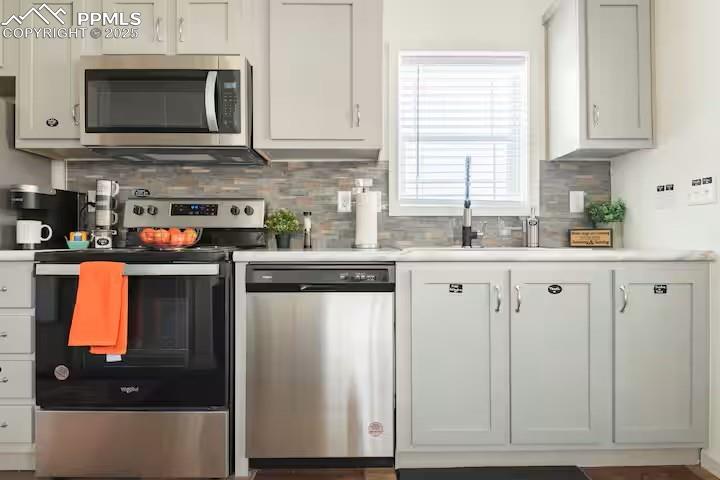 Image 8 of 27: Kitchen with decorative backsplash, white cabinets, stainless steel applian