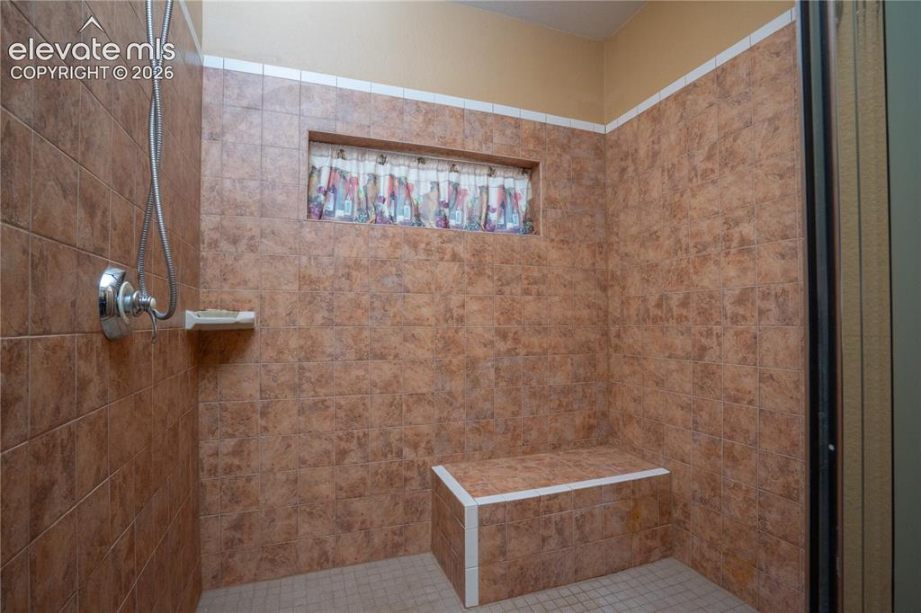 Image 20 of 47: This oversized tiled shower offers 2-shower heads and a bench