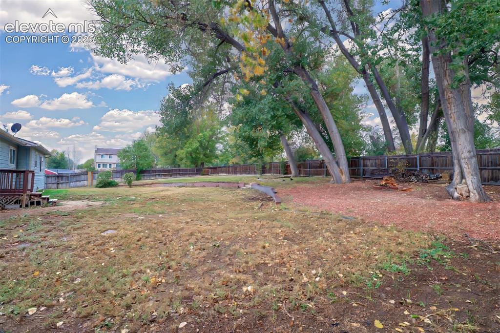 Image 25 of 34: Backyard featuring mature trees, wood fencing, and a terraced earth elevati