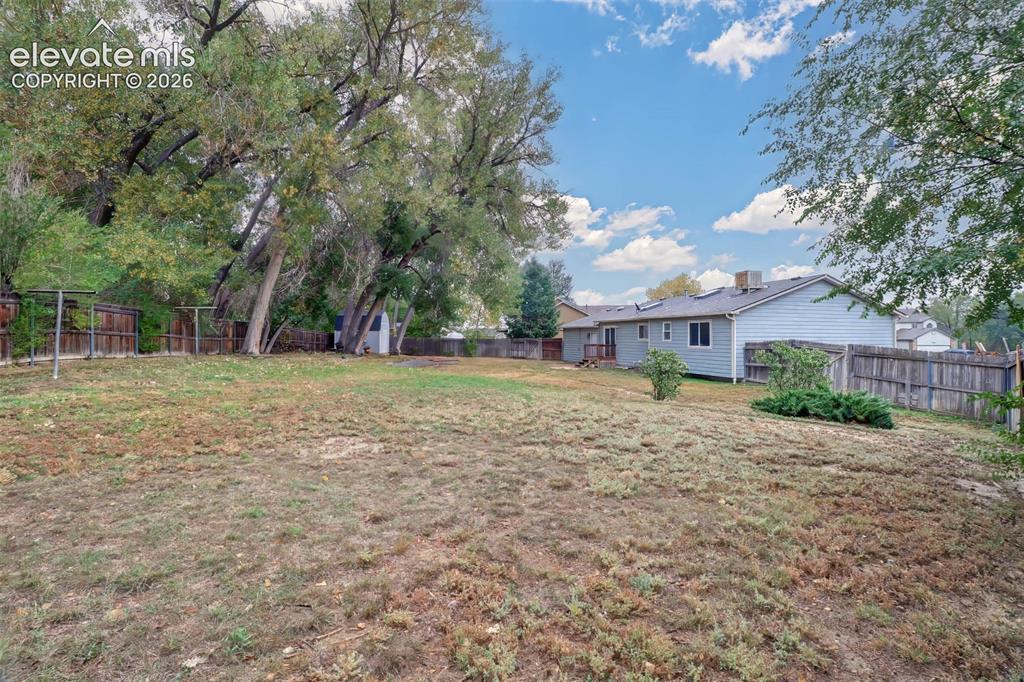 Image 28 of 34: Expansive backyard featuring mature trees, wood privacy fencing, and a deta