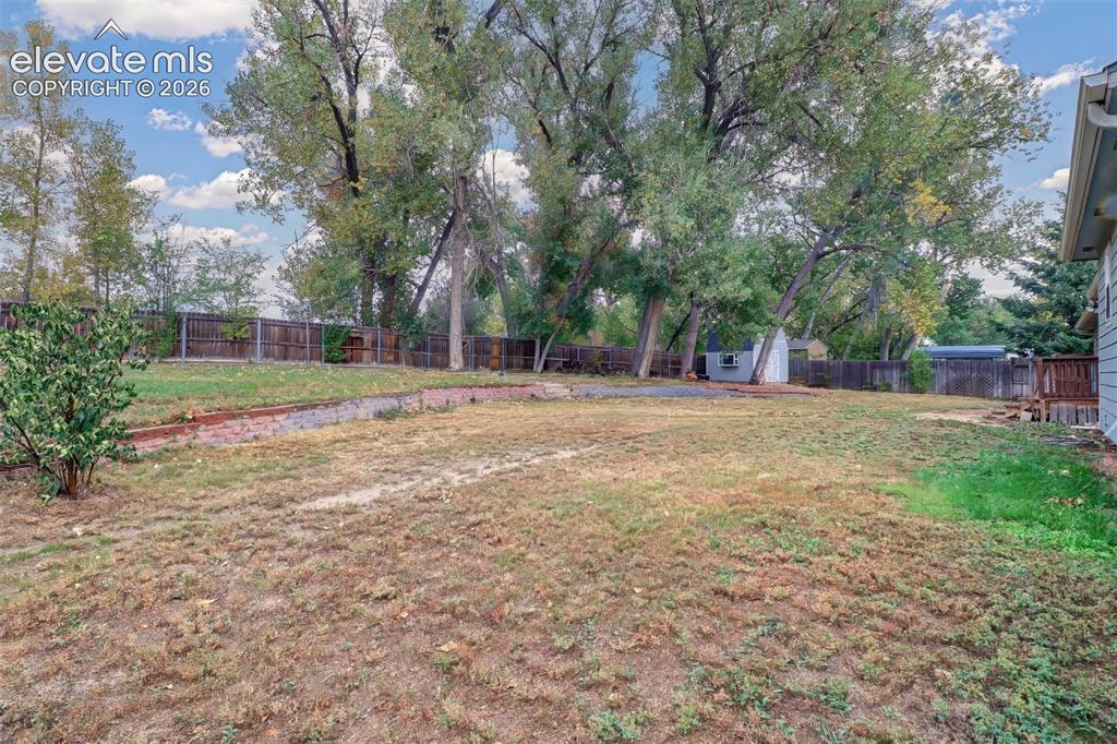 Image 29 of 34: Expansive backyard featuring a tiered brick retaining wall, mature trees, p