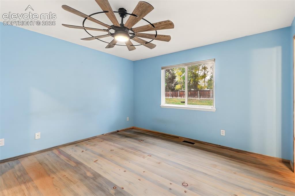 Image 8 of 34: Multi-tonal wood-finish flooring, large window, and a multi-blade ceiling f