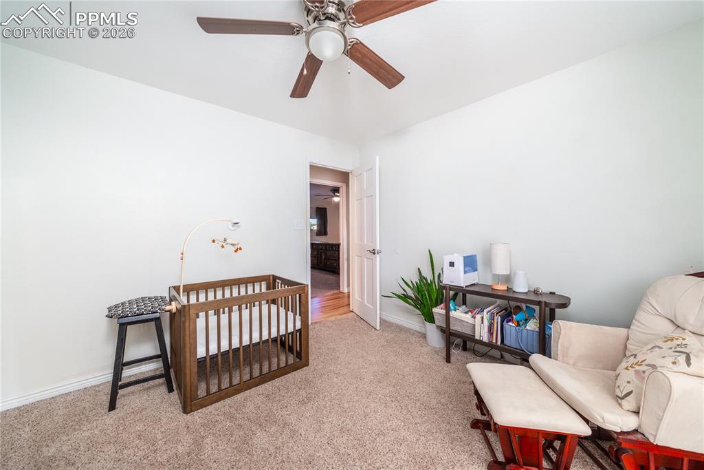 Image 15 of 48: Carpeted bedroom with a crib and a ceiling fan