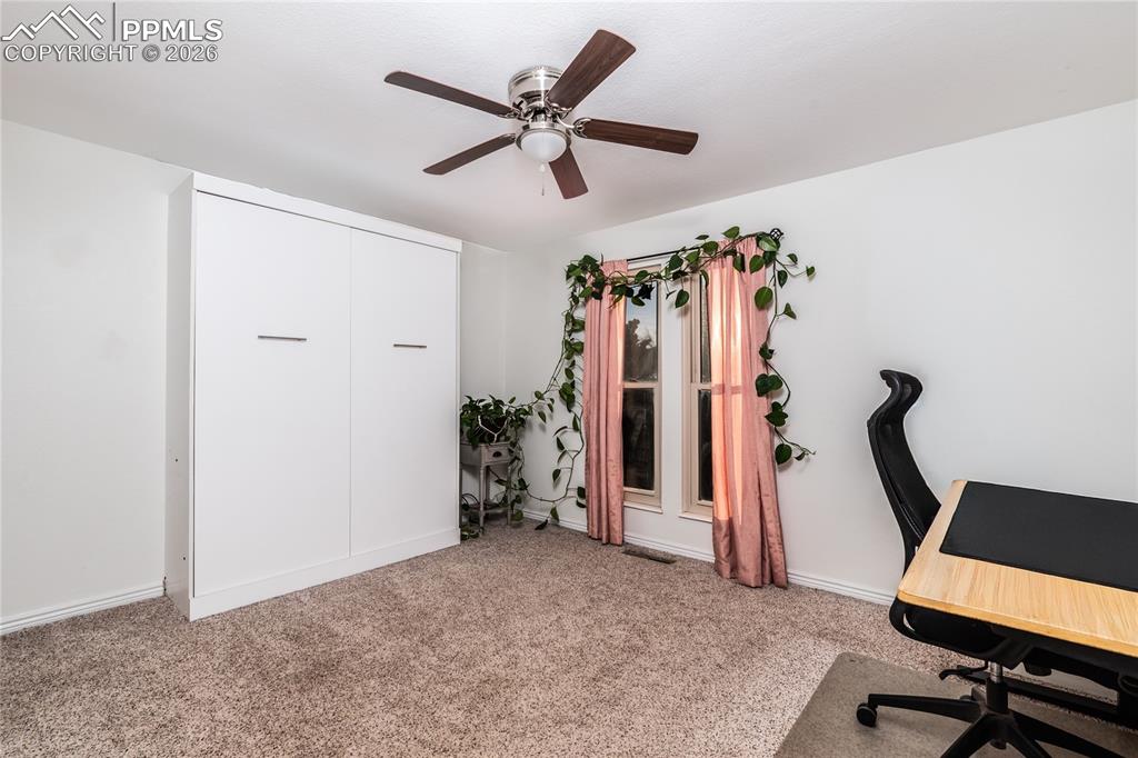 Image 16 of 48: Office space with light colored carpet and a ceiling fan
