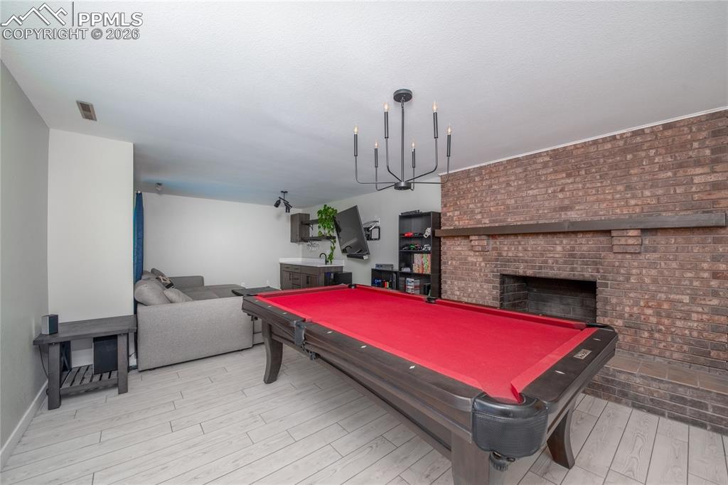 Image 22 of 48: Rec room featuring pool table, a brick fireplace, light wood-type flooring,