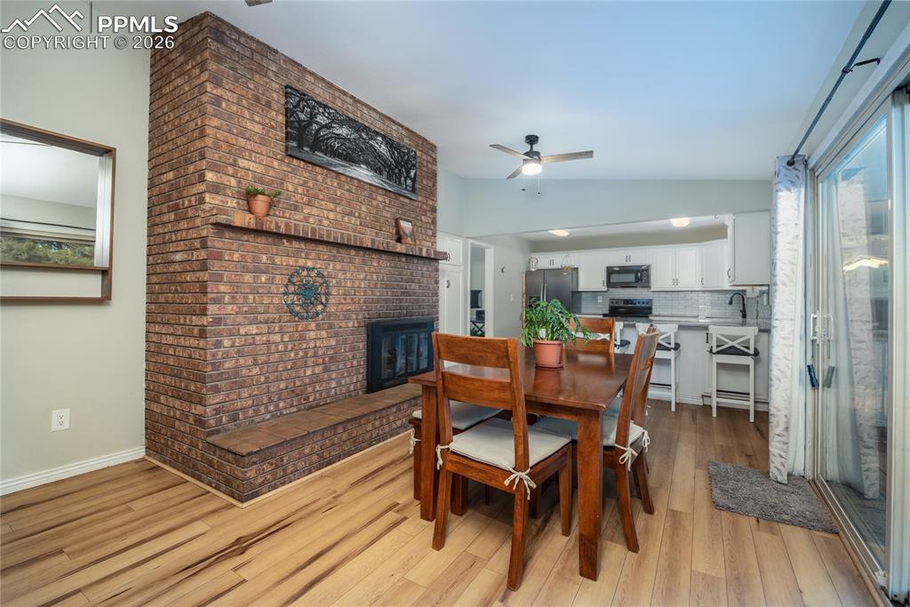 Image 9 of 48: Dining area featuring ceiling fan, lofted ceiling, a brick fireplace, and l