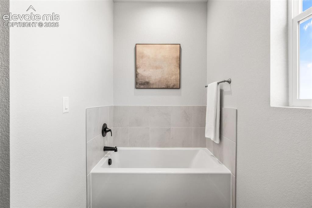 Image 22 of 40: Bathtub with matte black fixtures, light-toned wall tile surround, and a wi