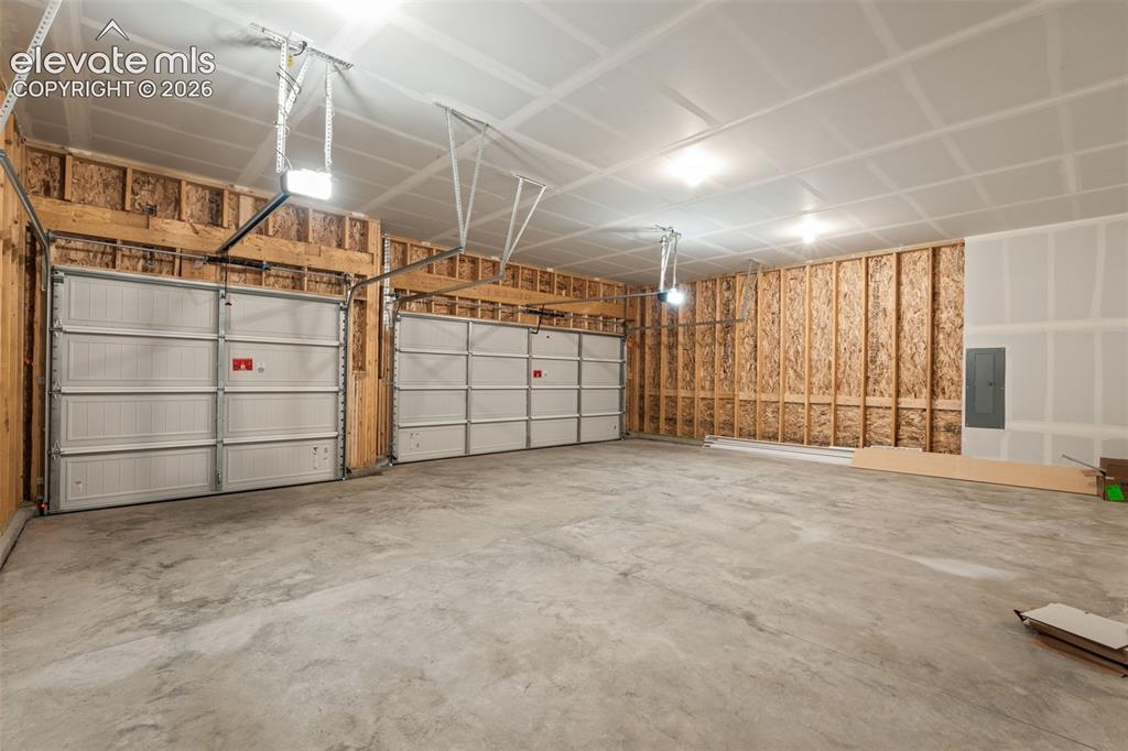 Image 32 of 40: Two white garage doors with automatic openers, exposed wood framing, and a 