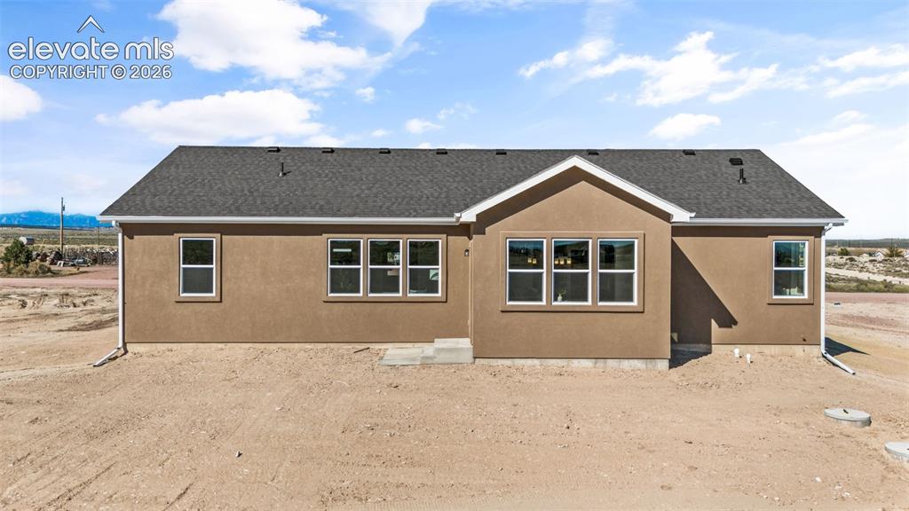 Image 34 of 40: Stucco exterior with a dark shingle roof, white trim, and multiple windows