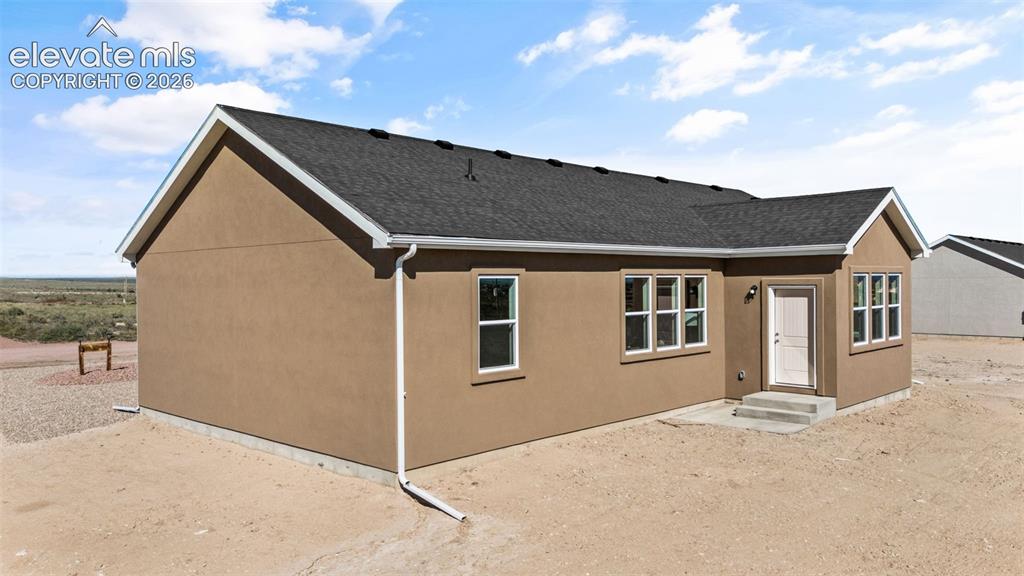 Image 35 of 40: Stucco exterior with a dark shingle roof, white window trim, and white gutt