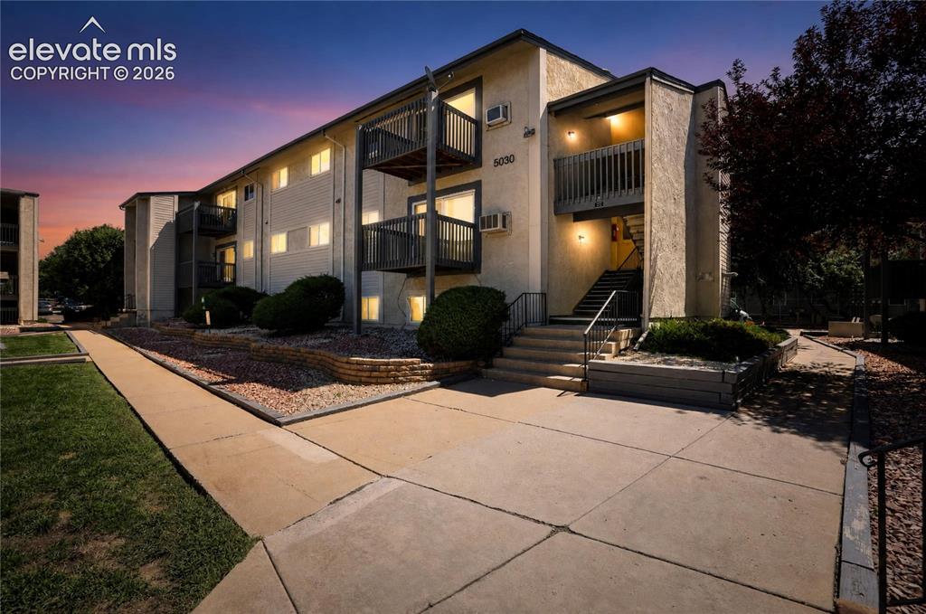 Caption: Multi-story building exterior with individual balconies, exterior staircases, and concrete pathways