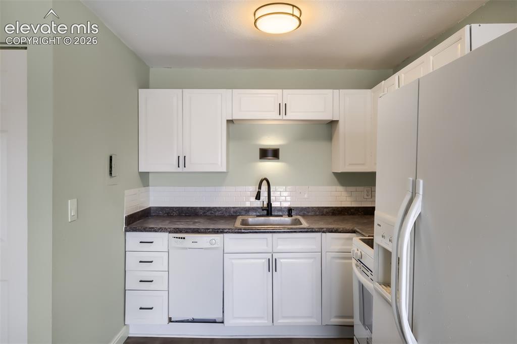 Image 10 of 38: White cabinetry with dark hardware, dark countertop, subway tile backsplash