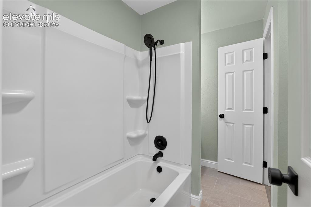 Image 15 of 38: Built-in bathtub with shower, matte black fixtures, and tiled flooring