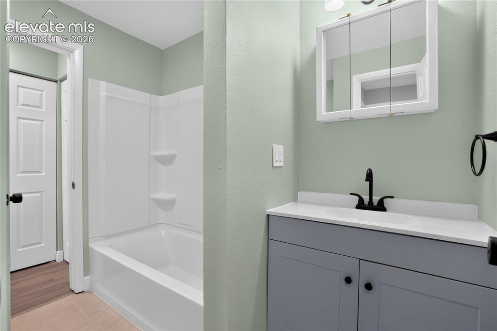 Image 22 of 38: Updated bathroom featuring soft sage-green walls, a gray vanity with black 