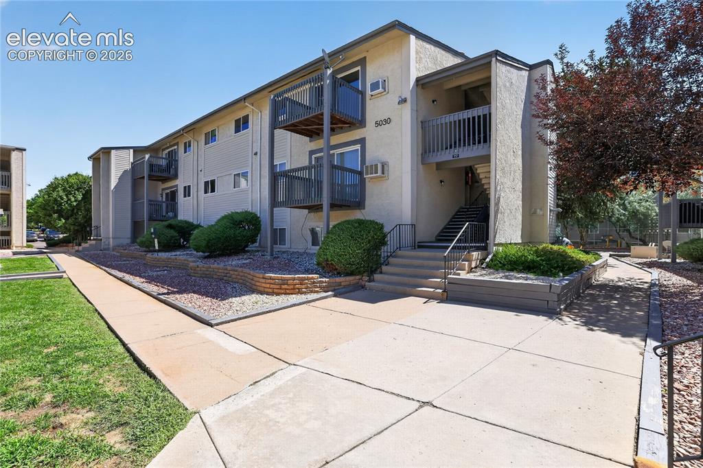 Image 25 of 38: Exterior building with multiple balconies, stucco siding, and concrete walk