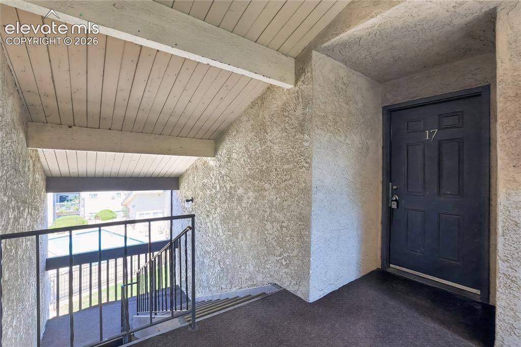 Image 3 of 38: Textured wall finish, wood-plank ceiling, dark panel door with house number
