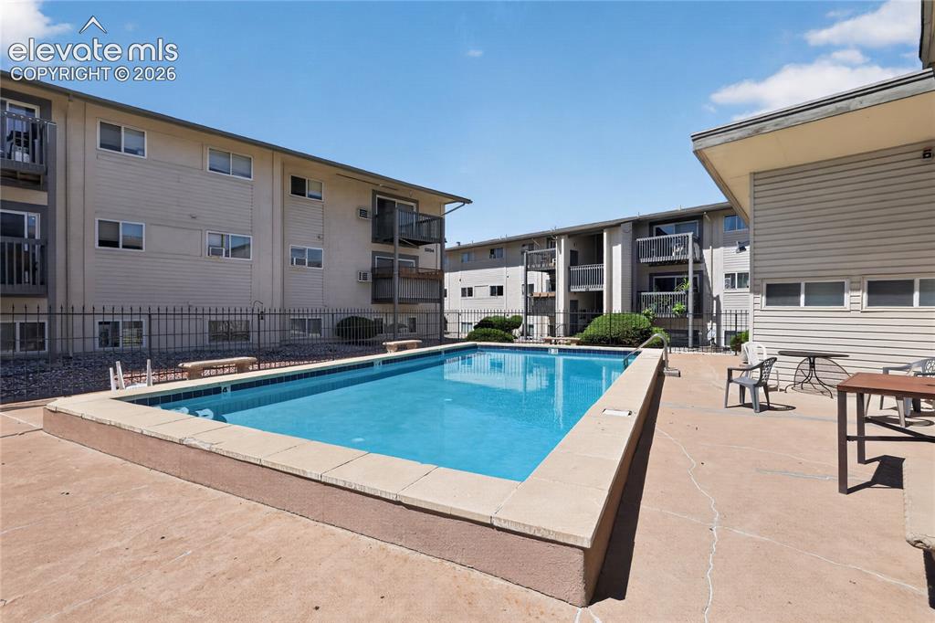 Image 30 of 38: Outdoor swimming pool with concrete decking, surrounded by multi-story resi