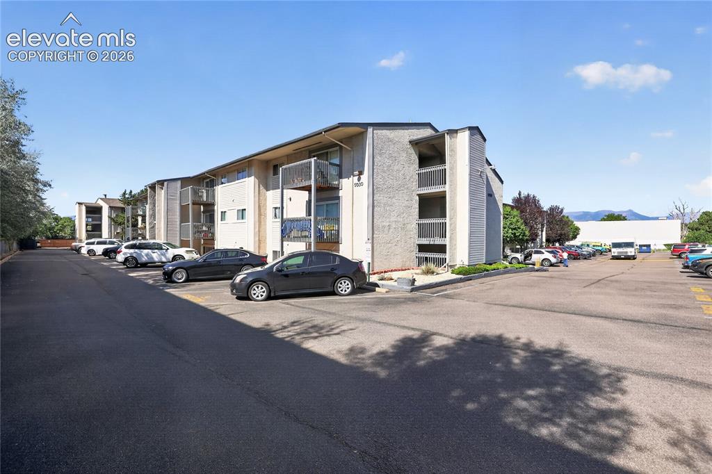 Image 31 of 38: Multi-story building with exterior balconies and a large parking area