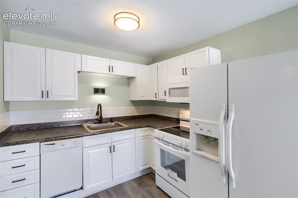 Image 8 of 38: Modern kitchen featuring white cabinetry with brushed nickel hardware, dark
