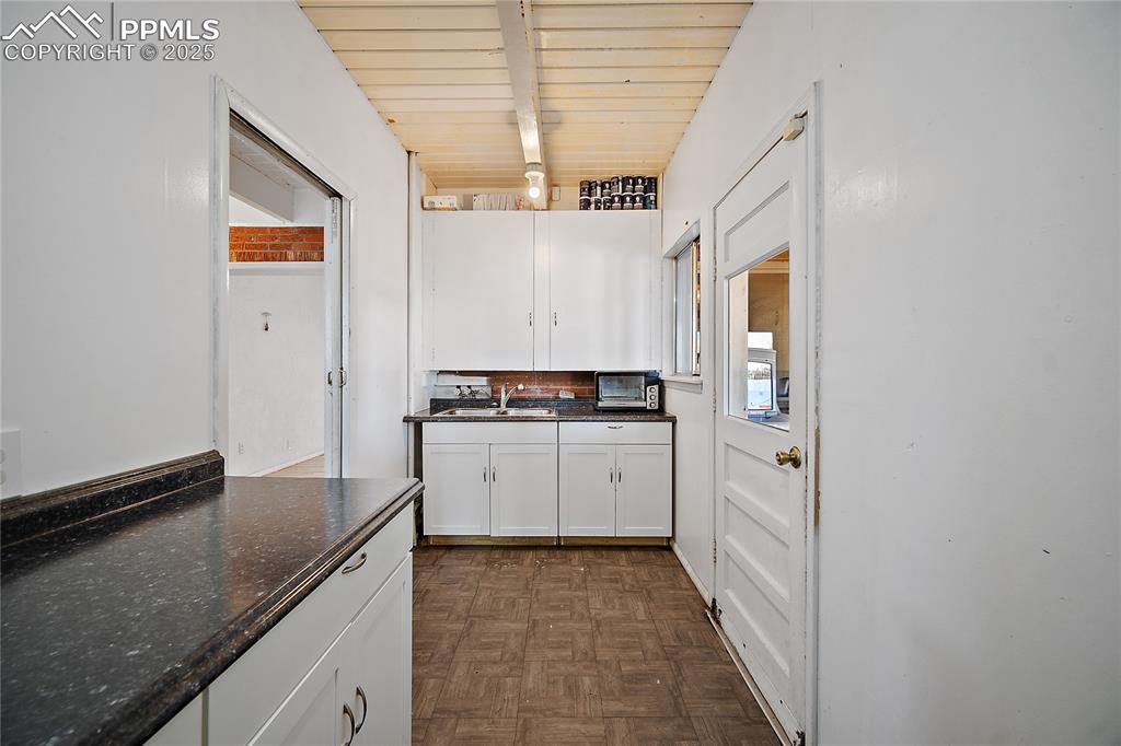 Image 15 of 31: Kitchen with dark countertops, white cabinets, and beam ceiling