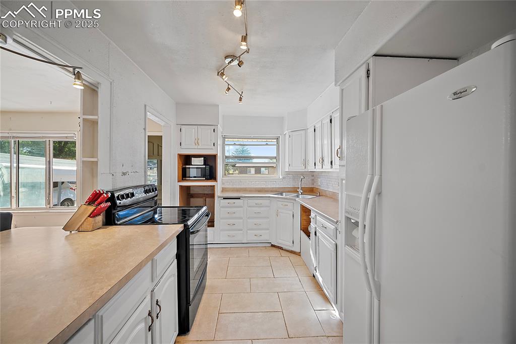 Image 4 of 31: Kitchen with stove, refrigerator, white cabinetry, light countertops, and l