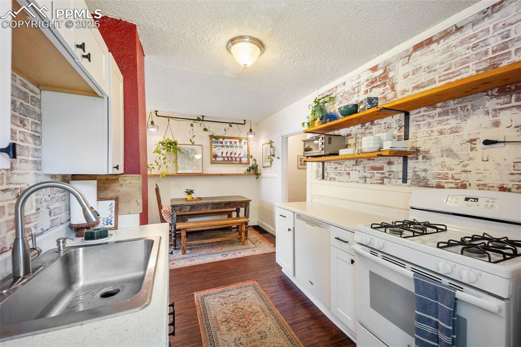 Image 19 of 41: Kitchen with brick wall, white cabinetry, white appliances, a textured ceil