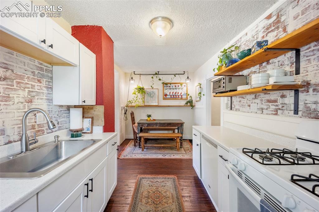 Image 21 of 41: Kitchen featuring white appliances, white cabinets, open shelves, brick wal