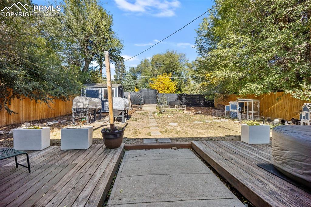 Image 27 of 41: Wooden deck featuring a patio, a fenced backyard, and a storage unit