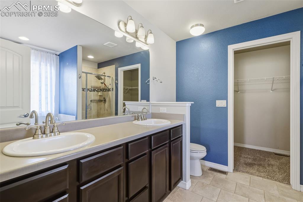 Image 16 of 27: Full bath featuring a walk in closet, a stall shower, double vanity, a text