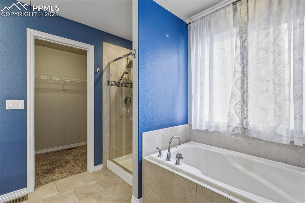 Image 17 of 27: Bathroom with a walk in closet, a textured wall, a garden tub, a stall show