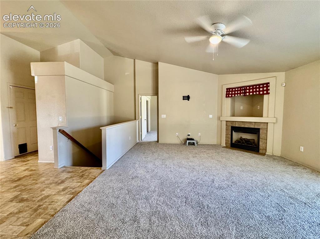 Image 10 of 39: Spacious carpeted room featuring a ceiling fan, a fireplace with a tiled he