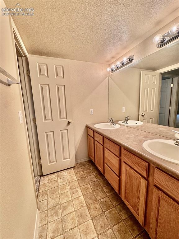 Image 25 of 39: Double vanity with wood-finish cabinetry, integrated sinks, and a large wal