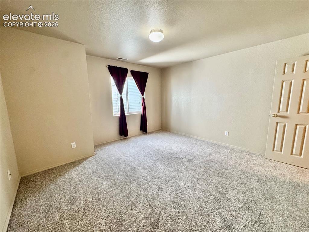 Image 30 of 39: Spacious interior room featuring textured carpeting, neutral wall paint, an