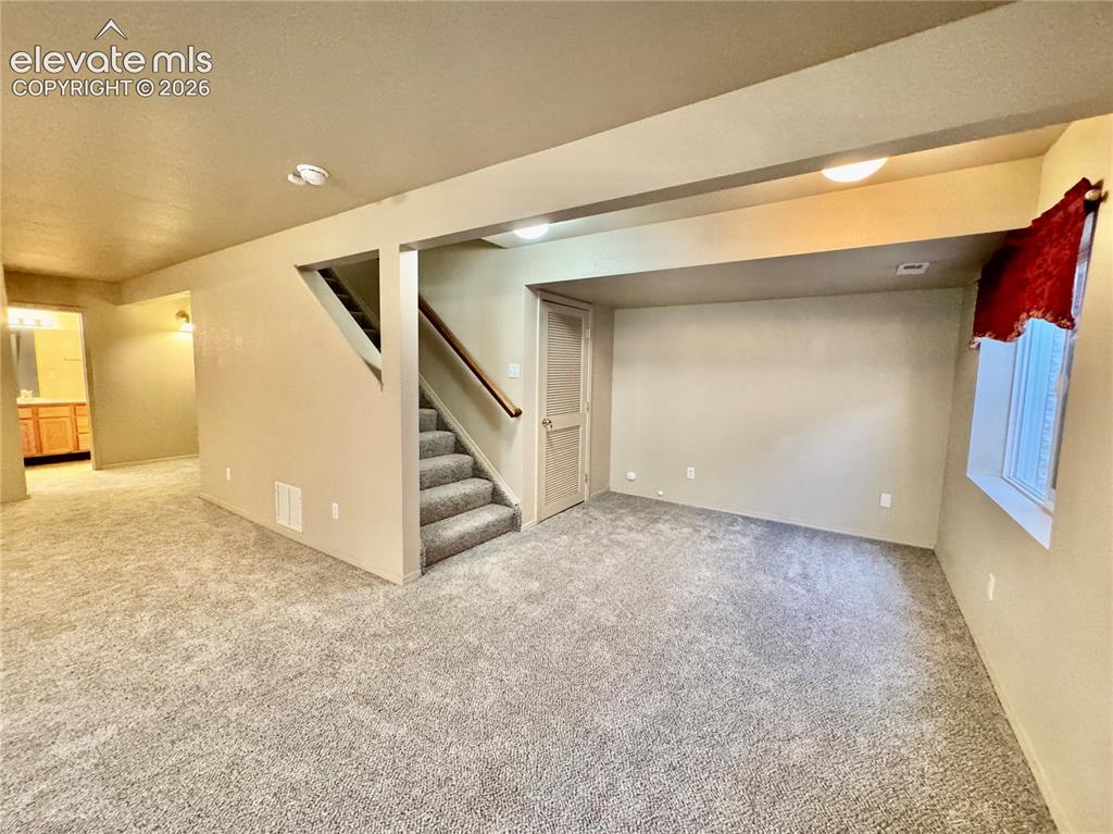 Image 32 of 39: Spacious carpeted area featuring an interior staircase with wooden handrail