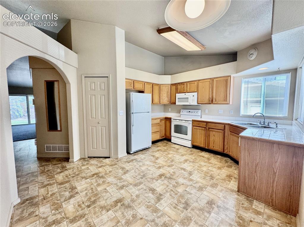 Image 8 of 39: Kitchen featuring wood cabinetry, white appliances, a tile countertop at th