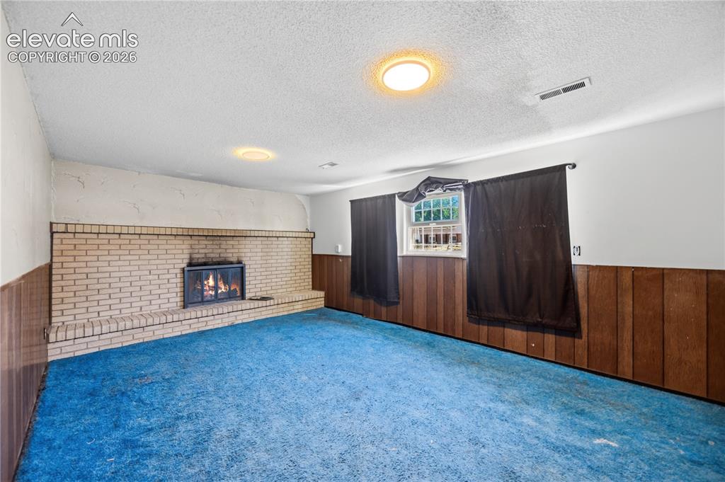 Image 26 of 35: Brick fireplace with a metal insert, wood paneling, and ceiling-mounted lig