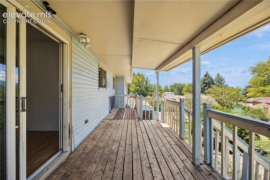 Image 30 of 35: Expansive wooden deck with railing, covered patio space, and sliding glass 