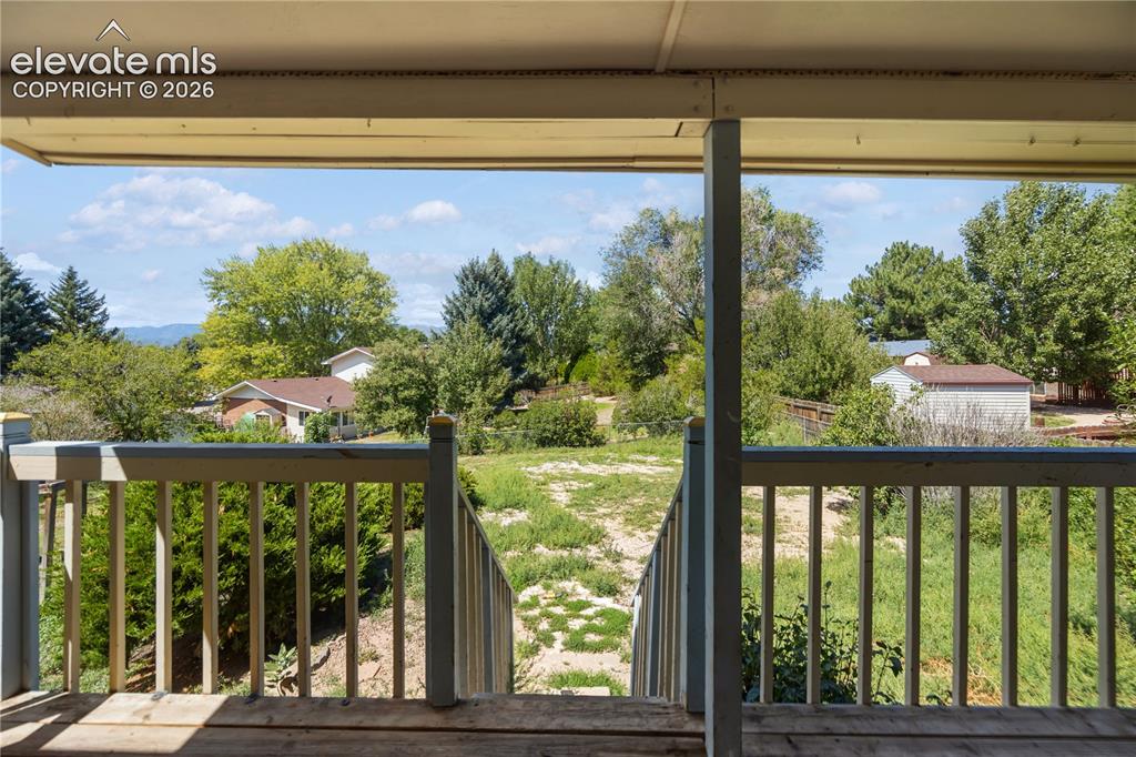 Image 33 of 35: Covered wood-finish deck with railing overlooking an expansive grassy area