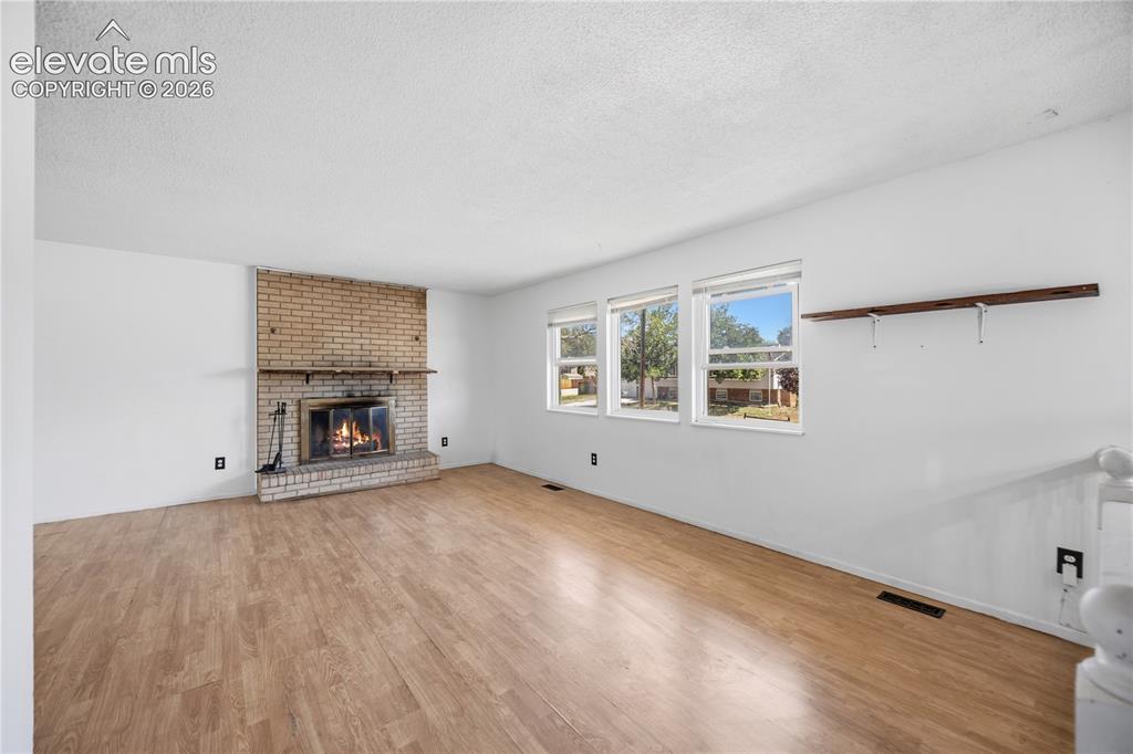 Image 6 of 35: Brick fireplace with hearth, wood-finish flooring, multiple windows, and a 