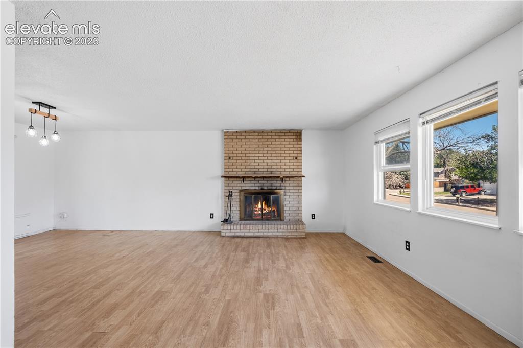 Image 7 of 35: Spacious room featuring wood-finish flooring, a brick fireplace with a wood