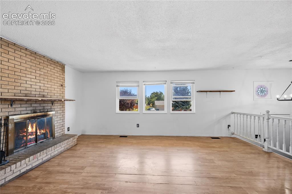 Image 8 of 35: Brick-surround fireplace with hearth, wood-finish flooring, multiple window
