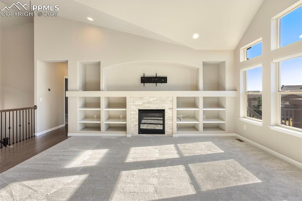 Image 11 of 48: Unfurnished living room featuring a tile fireplace, high vaulted ceiling, b
