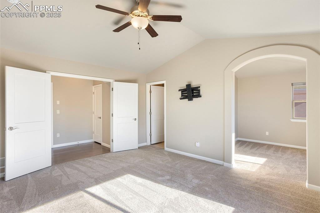 Image 19 of 48: Unfurnished bedroom featuring light carpet, vaulted ceiling, arched walkway
