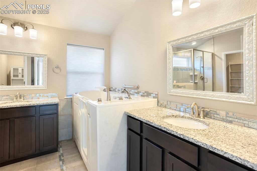 Image 24 of 48: Bathroom with two vanities, light tile patterned floors, a stall shower, a
