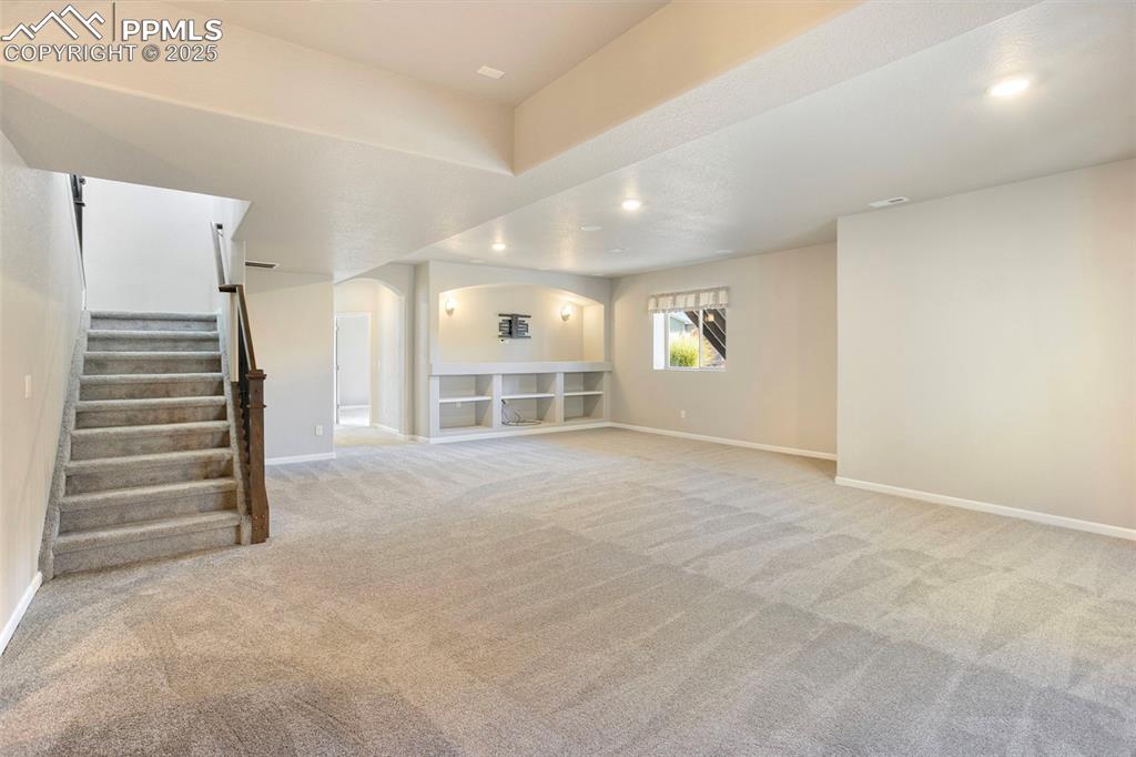 Image 31 of 48: Unfurnished living room featuring light carpet, arched walkways, stairway,