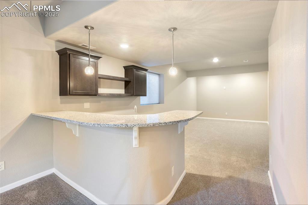 Image 36 of 48: Kitchen with dark brown cabinets, light carpet, a kitchen bar, open shelves