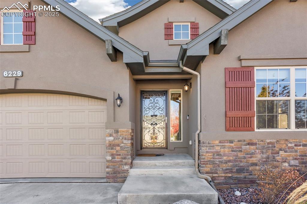 Image 4 of 48: Doorway to property featuring stone siding, a garage, and stucco siding