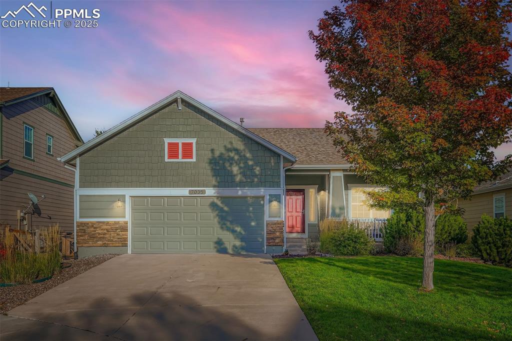 Caption: View of front of house with stone siding, concrete driveway, and a front lawn